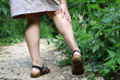 Woman with bare legs holding on to the shin standing on a path near tall stinging nettle. Leisure in countryside in summer, danger for skin