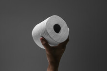One Hand Holding A Roll Of Toilet Paper With Spotlight Effect And Isolated Dark Grey Background