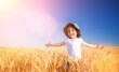 Happy girl walking in golden wheat, enjoying the life in the field. Nature beauty, sunny blue sky and field of wheat. Family outdoor lifestyle. Freedom concept. Cute little girl in summer field