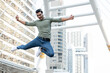 © Atstock Productions - Full length of carefree Indian young man with arms outstretched jumping in mid-air while enjoying music over headphones against modern buildings in city