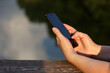© Oleg - Female hands with smartphone close up on lake background. Woman using mobile phone in summer park