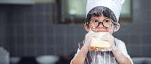 Cute Asian Boy Wearing Chef Hat Apron Eating Bread In Kitchen At Home