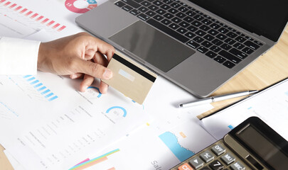 Businessman holding a credit card to pay taxes on a laptop. and a calculator on the desk. tax management concepts