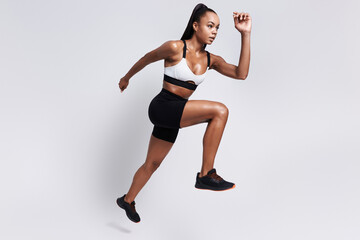 Wall Mural - Concentrated young African woman in sports clothing running against white background