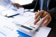 © crizzystudio - Asian male finance staff is calculating by using a calculator. Investment results to report to his boss at the meeting. On the table in the office, the concept of calculating investment results