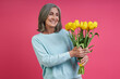 Leinwandbild Motiv Happy senior woman looking at the bunch of tulips while standing against pink background