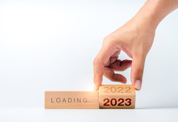 Canvas Print - Loading to 2023 happy new year. Hand flipping the 2022 to 2023 year numbers calendar on wooden cube blocks isolated on white background to prepare for new year change and start new business target.