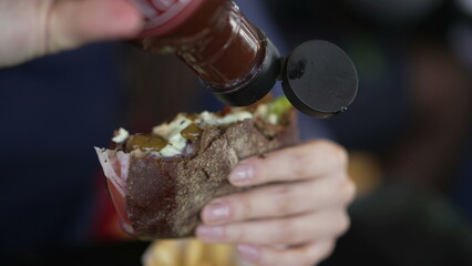 Closeup hand putting ketchup sauce on burger. Person adding hot sauce on hamburger