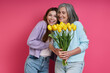 Leinwandbild Motiv Happy mother holding tulips while her adult daughter standing near and against pink background