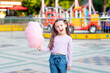 © Any Grant - a child girl in an amusement park in the summer eats cotton candy near the carousels, the concept of summer holidays and school holidays