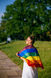 © teksomolika - Young woman with lgbt pride flag walking in the park.