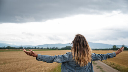 Young woman standing in beautiful nature of wheat fields with her arms spread widely