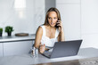 © F8  \ Suport Ukraine - Attractive young woman working typing on laptop computer and talking on mobile phone sitting in kitchen with modern interior.