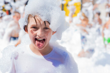 happy little boy with foam on his head, in wet clothes at a foam party or holiday on a sunny hot summer day

