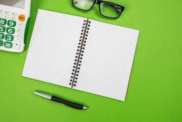 Top view of a blank white notepad with a calculator, glasses and a pen