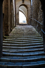 Wall Mural - A steep, paved street with the stairs and a stone gate