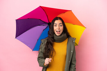 Wall Mural - Young woman holding an umbrella isolated on pink background with surprise facial expression