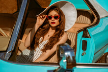 Fashion Portrait Of Confident Elegant Luxury Woman Wearing Red Sunglasses, White Wide Brim Hat, Striped Linen Jumpsuit, Posing In The Retro Car. Copy, Empty Space For Text