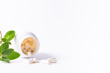 Wall Mural - White medical capsules in plastic jar on white background with fresh green leaves. Natural herbal medicine concept.