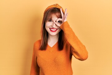 Sticker - Redhead young woman wearing casual orange sweater doing ok gesture with hand smiling, eye looking through fingers with happy face.