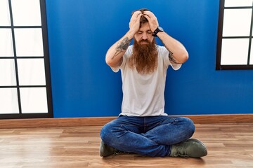 Sticker - Redhead man with long beard sitting on the floor at empty room suffering from headache desperate and stressed because pain and migraine. hands on head.