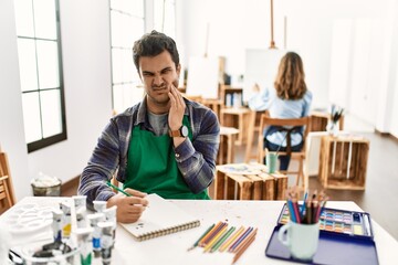 Poster - Young artist man at art studio touching mouth with hand with painful expression because of toothache or dental illness on teeth. dentist concept.