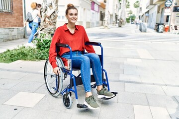 Wall Mural - Young brunette woman sitting on wheelchair outdoors looking positive and happy standing and smiling with a confident smile showing teeth