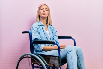 Wall Mural - Beautiful blonde woman sitting on wheelchair looking at the camera blowing a kiss on air being lovely and sexy. love expression.