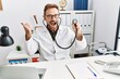 © Krakenimages.com - Middle age man with beard wearing doctor uniform holding stethoscope pointing thumb up to the side smiling happy with open mouth
