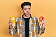 © Krakenimages.com - Young hispanic man eating doughnut and drinking coffee in shock face, looking skeptical and sarcastic, surprised with open mouth