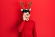 © Krakenimages.com - Young hispanic man wearing cute christmas reindeer horns covering one eye with hand, confident smile on face and surprise emotion.