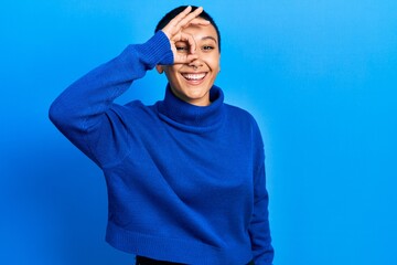 Sticker - Beautiful hispanic woman with short hair wearing turtleneck sweater doing ok gesture with hand smiling, eye looking through fingers with happy face.