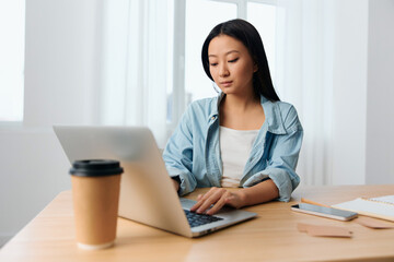 Focused serious young Asian cute female businesswoman type tax report on laptop in light office interior. Employee freelancer work at home. Lady corporation leader concept. Copy space Banner Offer