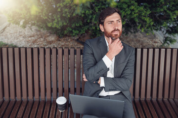 Sticker - Thoughtful male businessman working on laptop at lunchtime sitting on bench near office