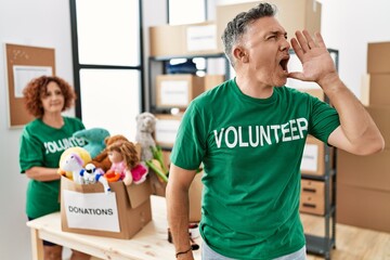 Poster - Middle age man wearing volunteer t shirt at donations stand shouting and screaming loud to side with hand on mouth. communication concept.