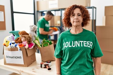 Wall Mural - Middle age woman wearing volunteer t shirt at donations stand relaxed with serious expression on face. simple and natural looking at the camera.