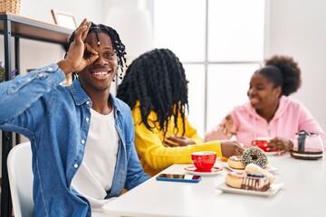 Sticker - Group of three young black people sitting on a table having coffee smiling happy doing ok sign with hand on eye looking through fingers