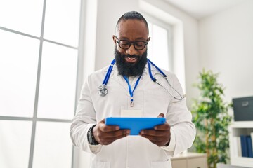 Poster - Young african american man wearing doctor uniform using touchpad at clinic