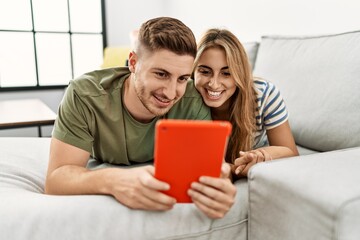 Wall Mural - Young hispanic couple using touchpad lying on the sofa at home.