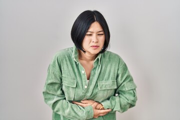 Sticker - Young asian woman standing over white background with hand on stomach because indigestion, painful illness feeling unwell. ache concept.