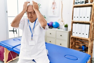 Poster - Senior physiotherapy man working at pain recovery clinic suffering from headache desperate and stressed because pain and migraine. hands on head.