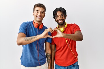 Wall Mural - Young hispanic brothers standing over isolated background wearing headphones smiling in love doing heart symbol shape with hands. romantic concept.