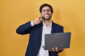 Sticker - Handsome latin man working using computer laptop smiling cheerful showing and pointing with fingers teeth and mouth. dental health concept.