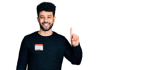 Poster - Young arab man with beard wearing hello my name is sticker identification smiling with an idea or question pointing finger with happy face, number one