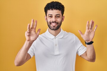 Sticker - Arab man standing over yellow background showing and pointing up with fingers number nine while smiling confident and happy.