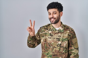 Sticker - Arab man wearing camouflage army uniform smiling looking to the camera showing fingers doing victory sign. number two.