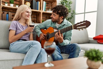 Sticker - Man playing spanish guitar to his girlfriend sitting on the sofa at home.