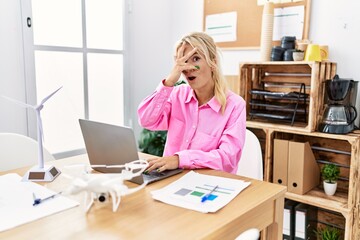 Poster - Young caucasian woman working at the office peeking in shock covering face and eyes with hand, looking through fingers with embarrassed expression.