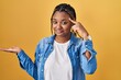 African american woman with braids standing over yellow background confused and annoyed with open palm showing copy space and pointing finger to forehead. think about it.