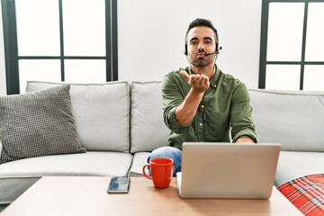 Poster - Young hispanic man with beard wearing call center agent headset working from home looking at the camera blowing a kiss with hand on air being lovely and sexy. love expression.